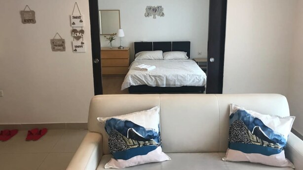 Ein Hotelzimmer mit einem Bett, einem Nachttisch, einer Lampe und einem Spiegel. Es gibt Wanddekorationen und einen Deckenventilator.