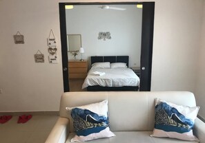 Ein Hotelzimmer mit einem Bett, einem Nachttisch, einer Lampe und einem Spiegel. Es gibt Wanddekorationen und einen Deckenventilator.