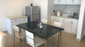 Eine kompakte Küche mit Esstisch, Glastischplatte, weißen Stühlen, einem Kühlschrank und weißen Schränken.