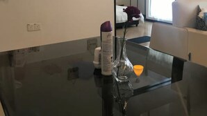 Ein modernes Zimmer mit einem Glastisch, einem Spiegel und Blick auf ein Bett und ein Fenster.