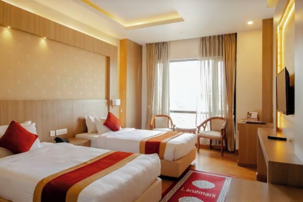 A hotel room with two beds, a desk, a chair, and a TV.