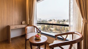 A room with a large window, two wooden chairs, a small round table with a fruit basket, and a wooden desk with a telephone. - Hotel Landmark Kathmandu (Kathmandu)