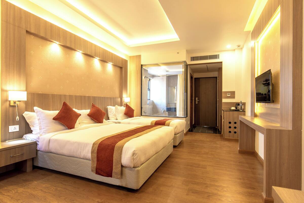 Ein Hotelzimmer mit zwei Betten, einem Fernseher, einem Schreibtisch und einem durchgegangenen Badezimmer.