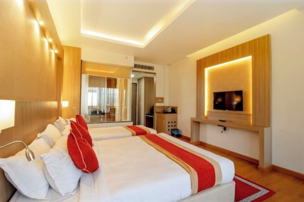 A hotel room with a large bed, a TV mounted on the wall, and a wooden headboard.