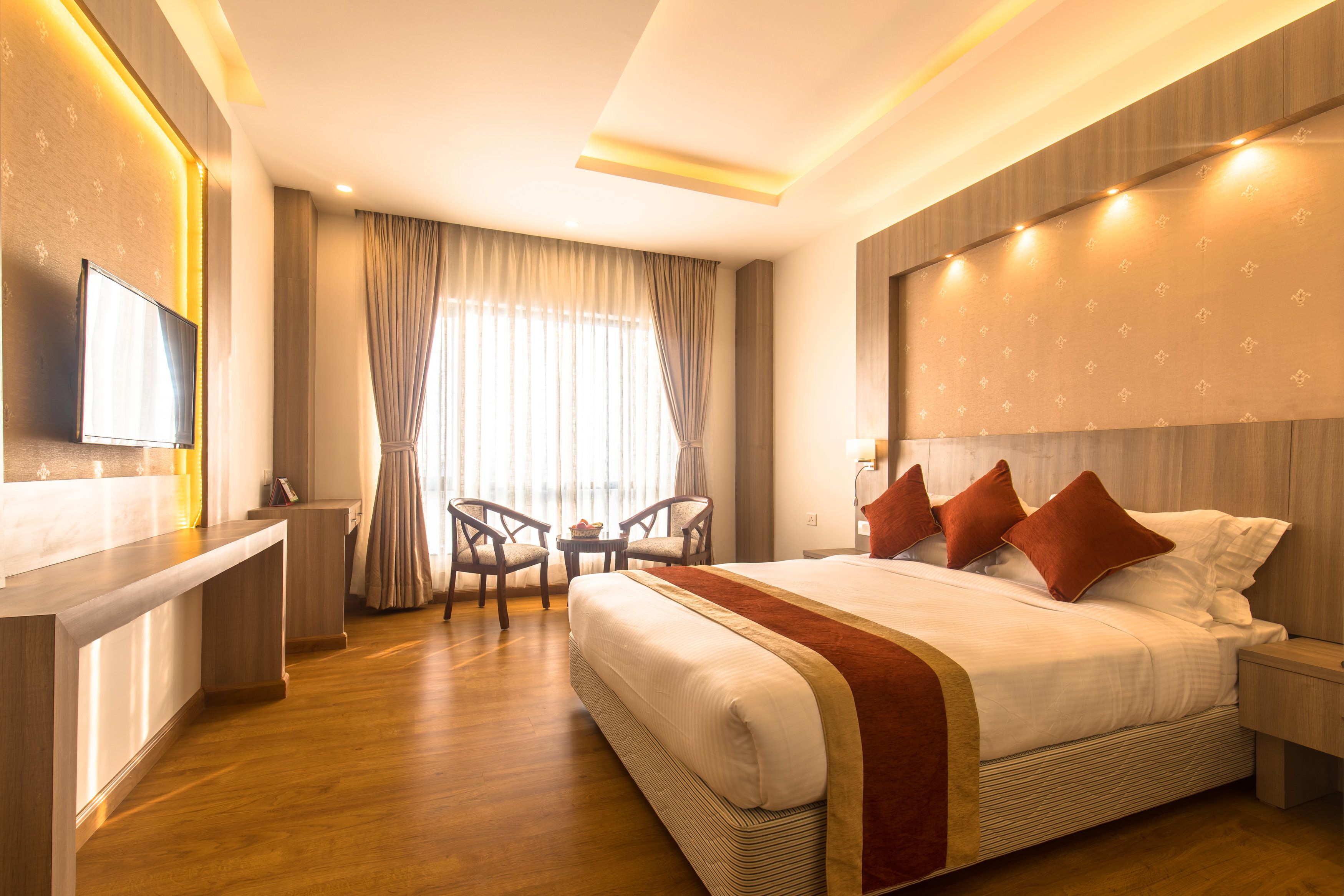 A hotel room with a large bed, a TV, a desk, and a seating area with chairs.