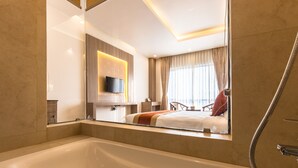 A modern bathroom with a large bathtub, a shower, and a mirror reflecting a bedroom with a bed and curtains. - Hotel Landmark Kathmandu (Kathmandu)