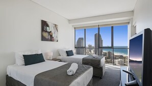 A hotel room with two beds, a large window with a city and beach view, and a television.