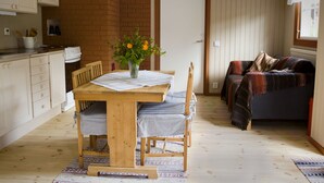 A cozy kitchen with a wooden table, chairs, and a vase of flowers. There is a dining table with a white tablecloth and a window with a view.