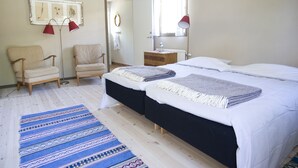 A bedroom with two beds, a chair, a dresser, a mirror, and a window with curtains.