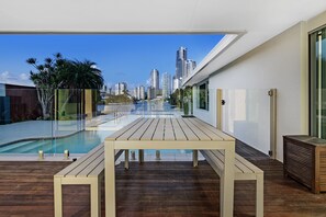 Een modern buitenzwembad met een houten terras, een overdekt zwembad en een stadsachtergrond.