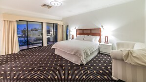 Ein Hotelzimmer mit einem großen Bett, einem Nachttisch, einem Sessel und einem Balkon mit Blick.
