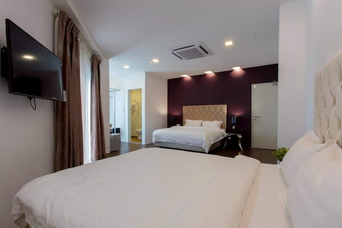 A hotel room with a large bed, a flat-screen TV mounted on the wall, a ceiling air conditioner, and a bathroom visible through an open door.