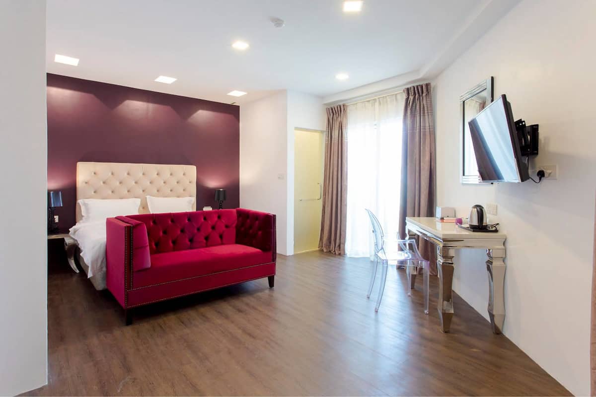 A modern hotel room with a red sofa, a bed with white linens, a small desk with a chair, and a mirror on the wall.