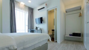 A hotel room with a large bed, a TV mounted on the wall, an air conditioning unit, a shower area, and a small shelf with items. - Aloha Hotel (Pontian)