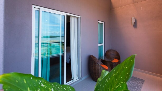 A modern room with a sliding glass door to a balcony, a wicker chair, and a small table. - Aloha Hotel (Pontian)