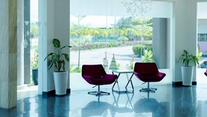 A modern lobby with two purple chairs, a small table, and potted plants. - Aloha Hotel (Pontian)