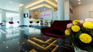 A modern hotel lobby with a reception desk, red seating, and a large floral arrangement. - Aloha Hotel (Pontian)