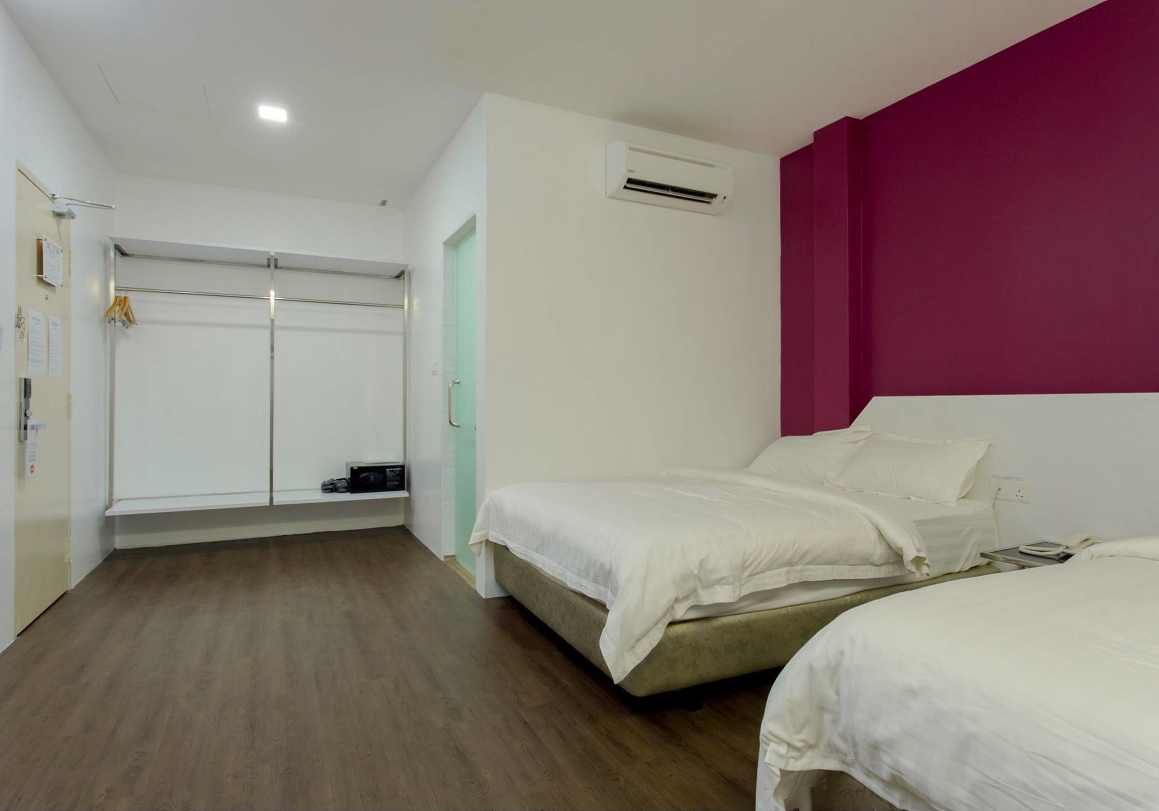 A hotel room with two beds, a wardrobe, and an air conditioning unit.