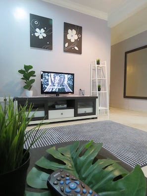 A living room with a flat-screen TV, a white entertainment unit, a potted plant, and a large green leaf. - GM Homestay Kelibang (Langkawi)