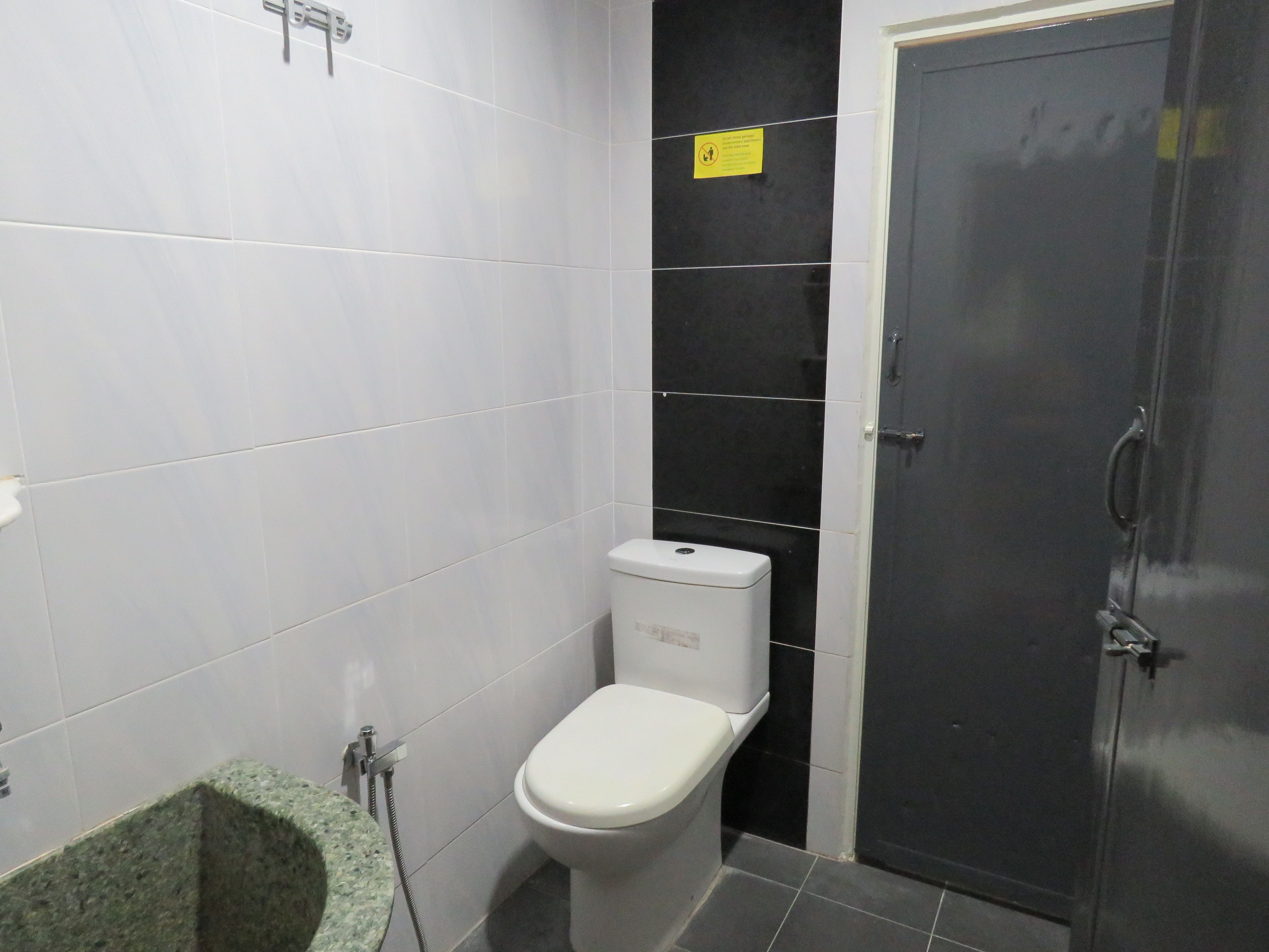 A bathroom with white tiles, a toilet, a sink with a green countertop, and a dark door.