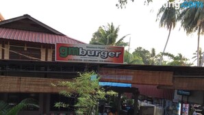 Un área de estar al aire libre con mesas y sillas, un letrero del restaurante 'gmburger', y un edificio con techo rojo al fondo.