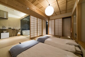 Une chambre de style japonais traditionnel, avec des tatamis, un futon, des portes coulissantes en papier de riz (shoji) et une petite cuisine moderne.