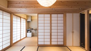 A traditional Japanese room with tatami flooring, sliding doors, and a kitchen area in the background. - Lica's Room (Kyoto)