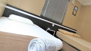 Une chambre d’hôtel comprenant un lit, une table de chevet, un canapé, un appareil de climatisation et une fenêtre avec des stores.