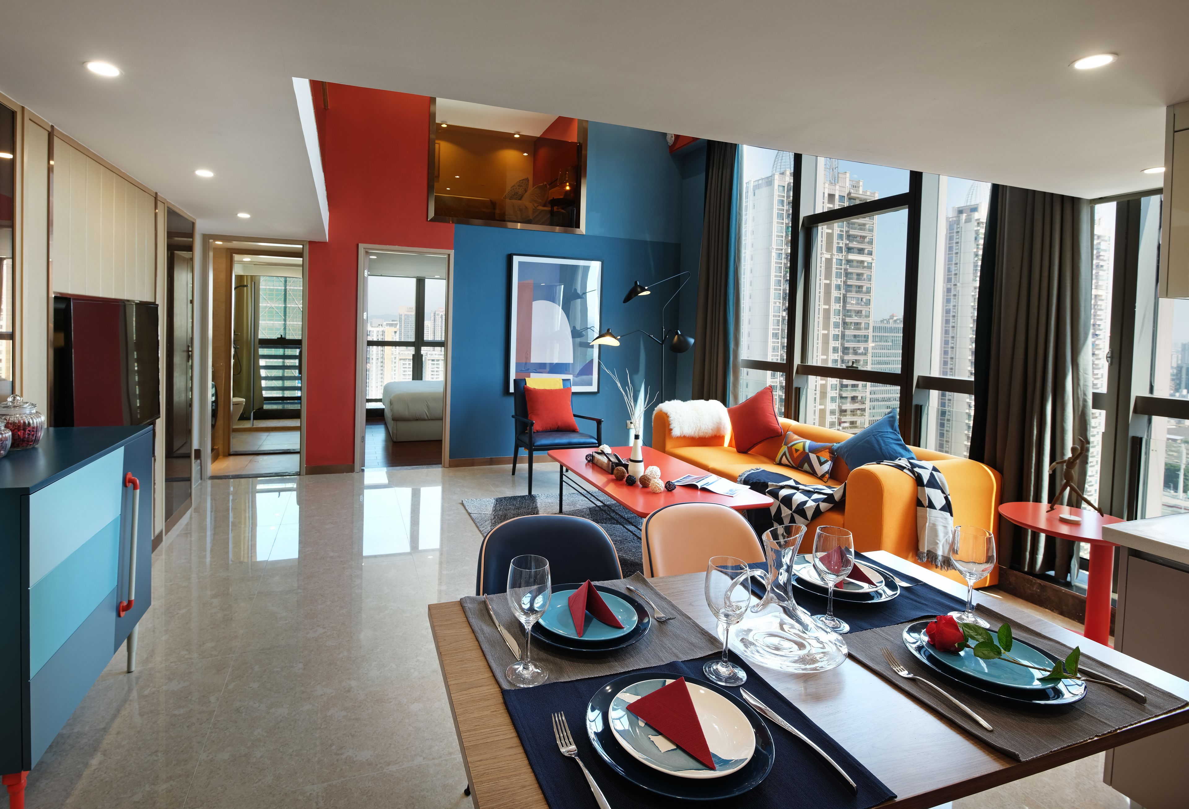A modern dining area with a table set for four, a sofa, and a city view through large windows.