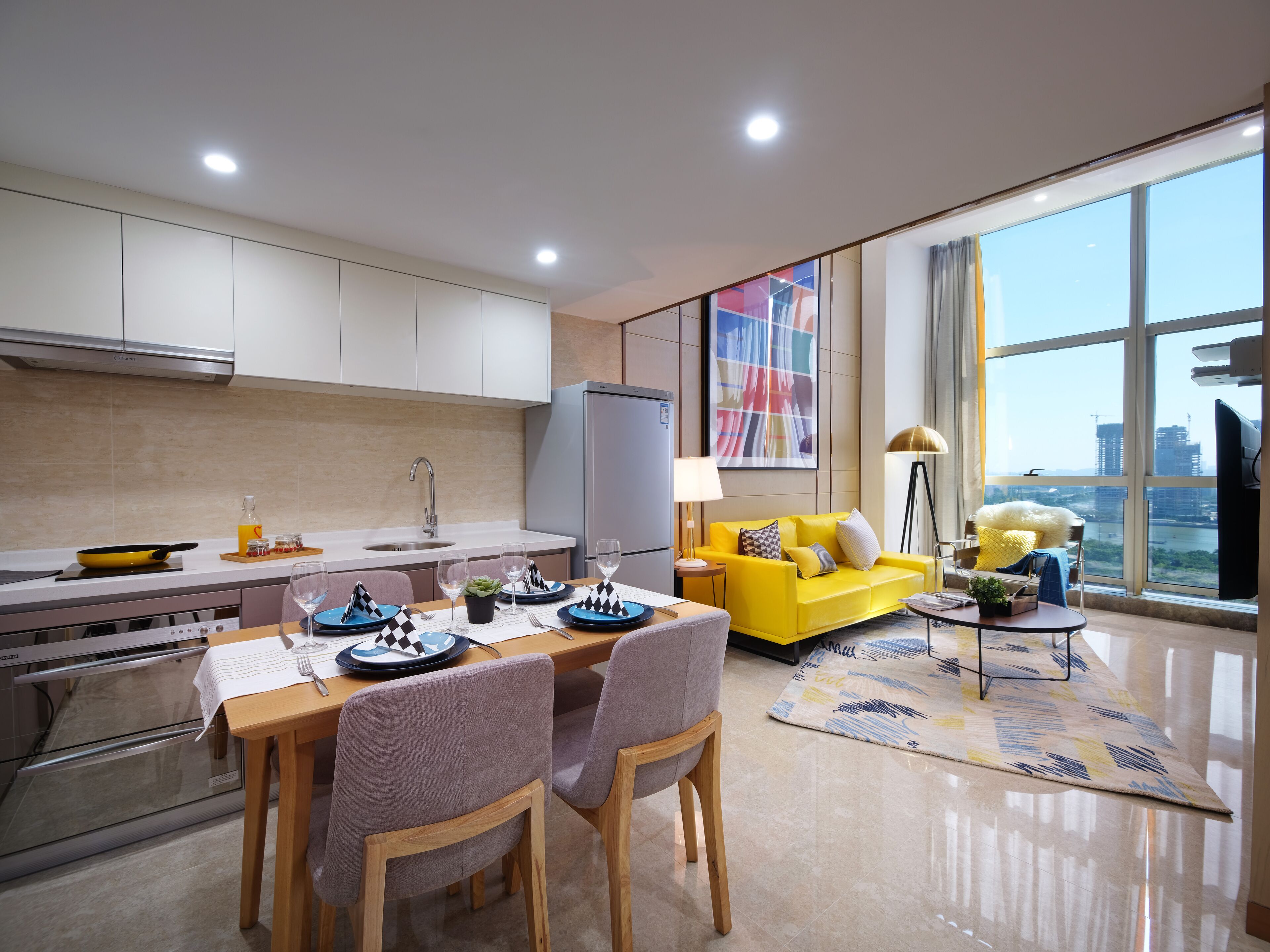 A modern kitchen with a dining area, a sofa, and a large window with a city view.