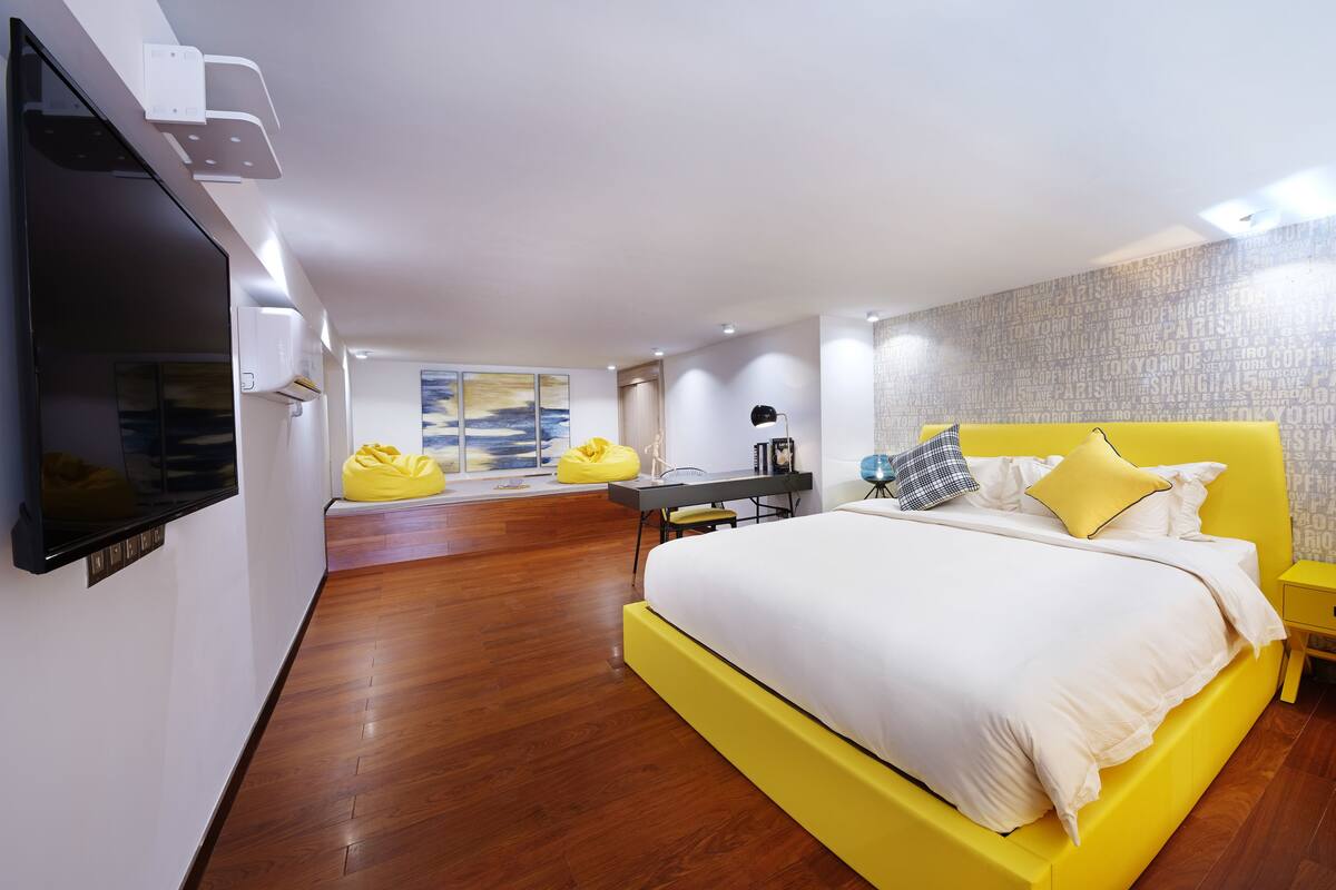 A modern bedroom with a large bed, a desk, and a TV.