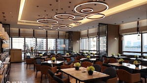 Een modern restaurant met meerdere eettafels en stoelen, grote ramen met uitzicht op de stad, en een decoratief plafond met ronde lichtarmaturen.