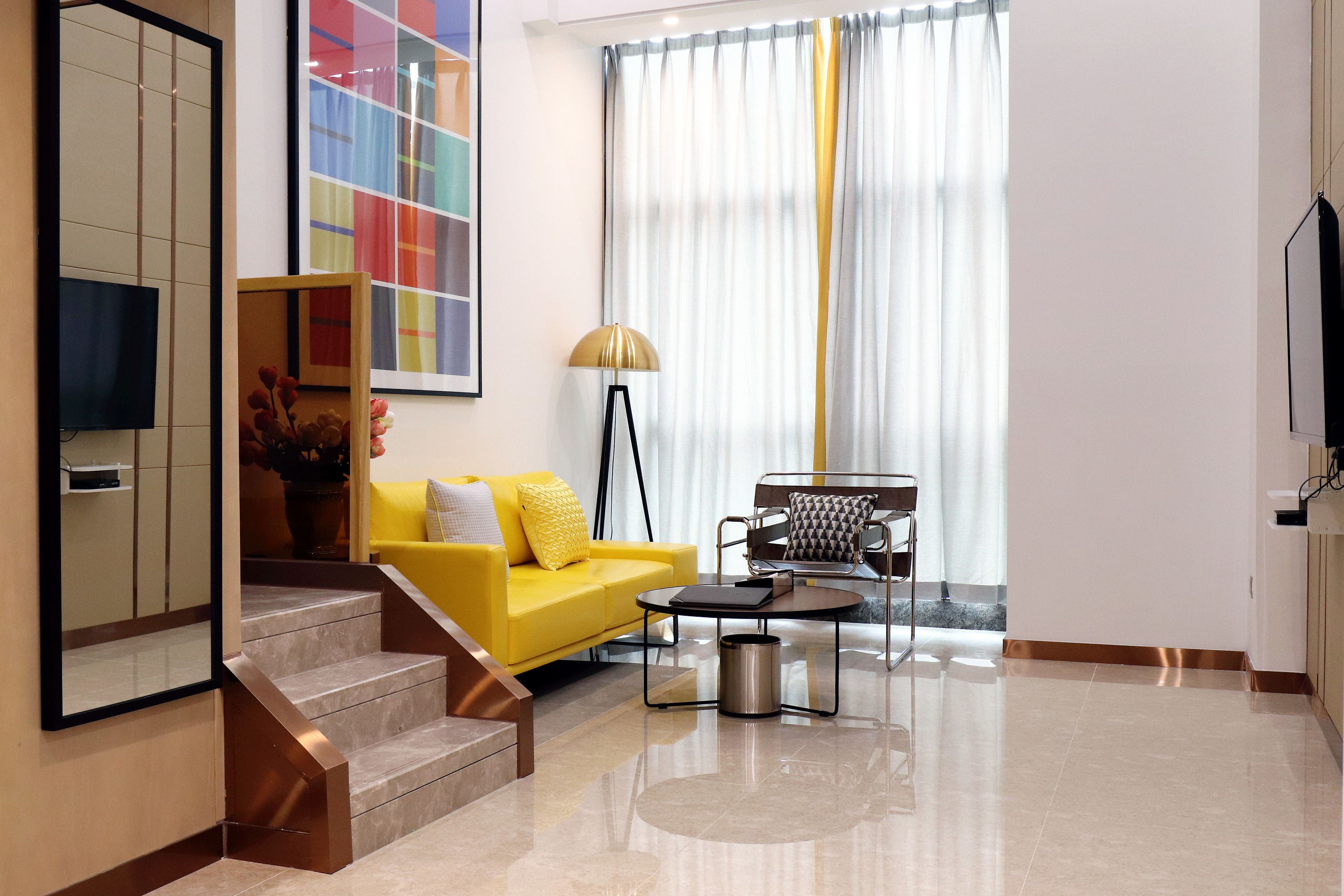 A modern living room with a yellow sofa, a coffee table, a lamp, and a TV.