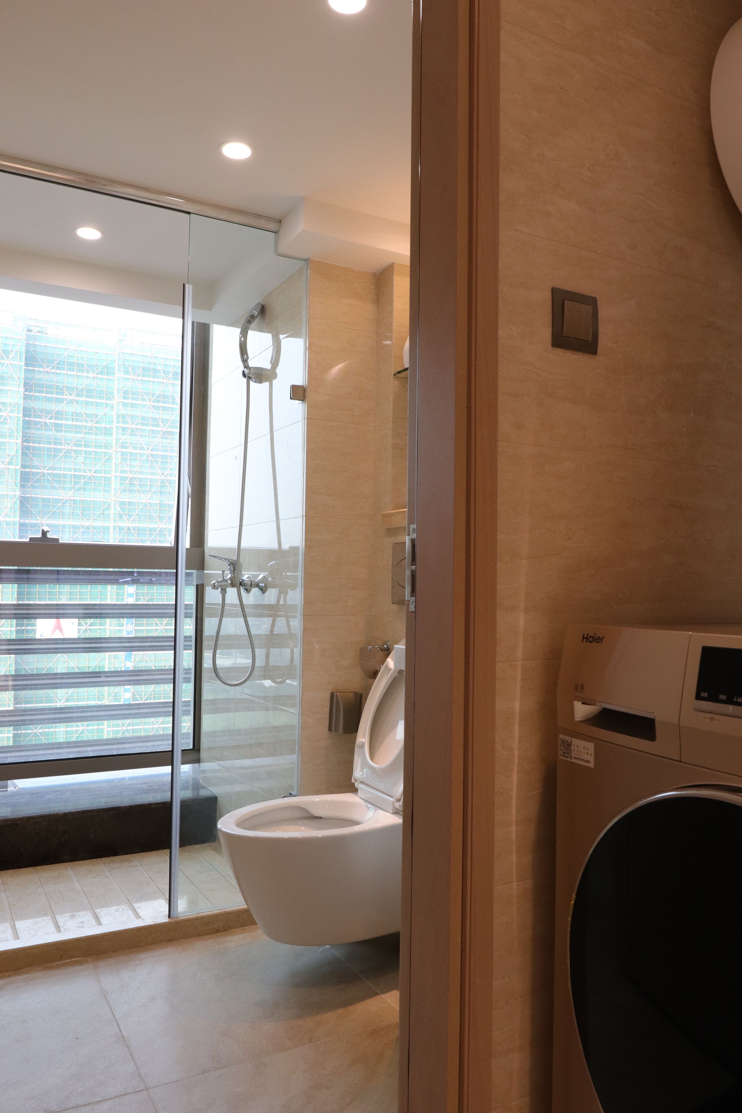 A modern bathroom with a glass shower enclosure, a toilet, and a built-in washing machine.
