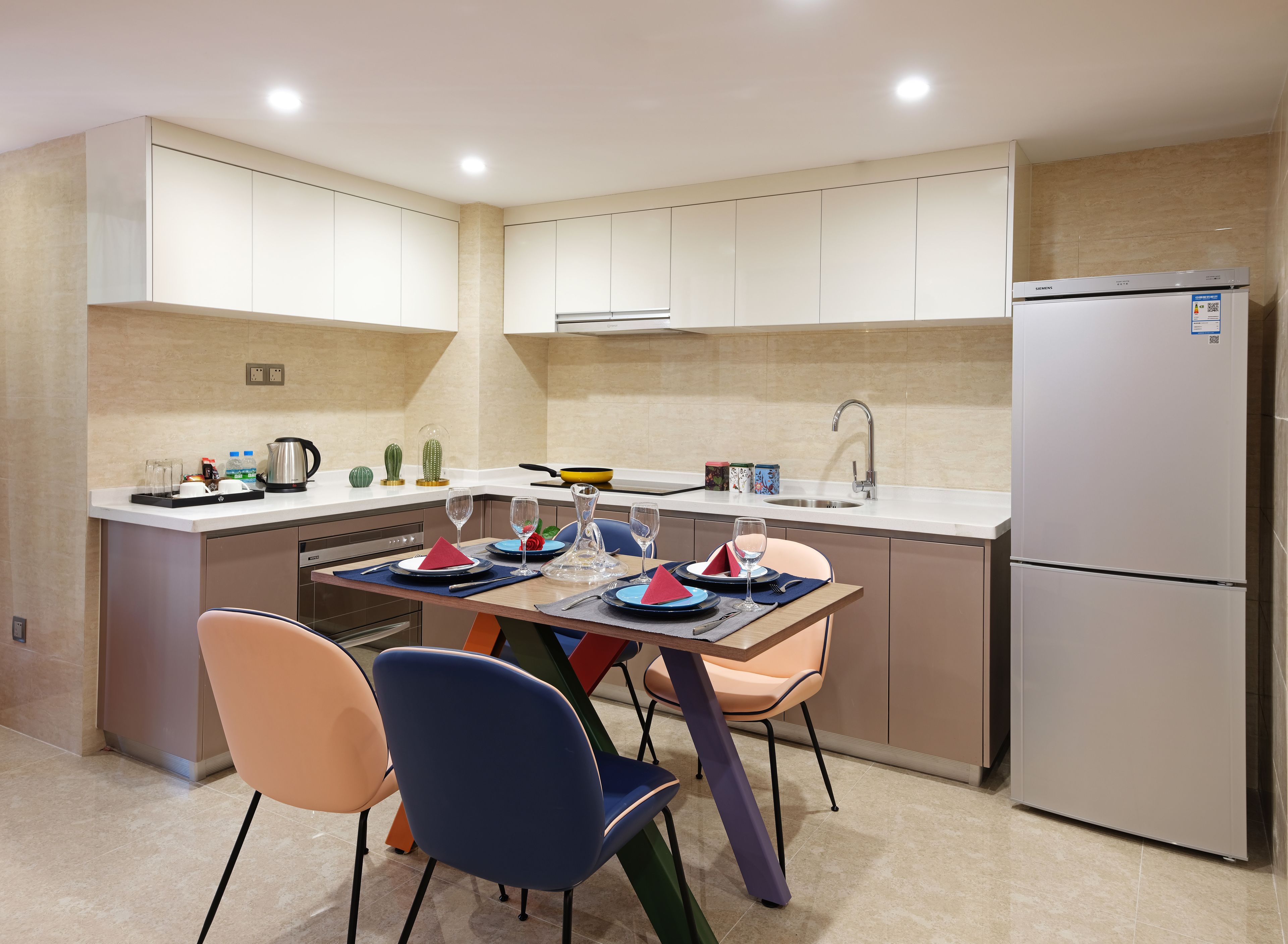 A modern kitchen with a dining area, featuring a stainless steel refrigerator, a built-in oven, and a sink.