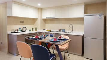 A modern kitchen with a dining area, featuring a stainless steel refrigerator, a built-in oven, and a sink.