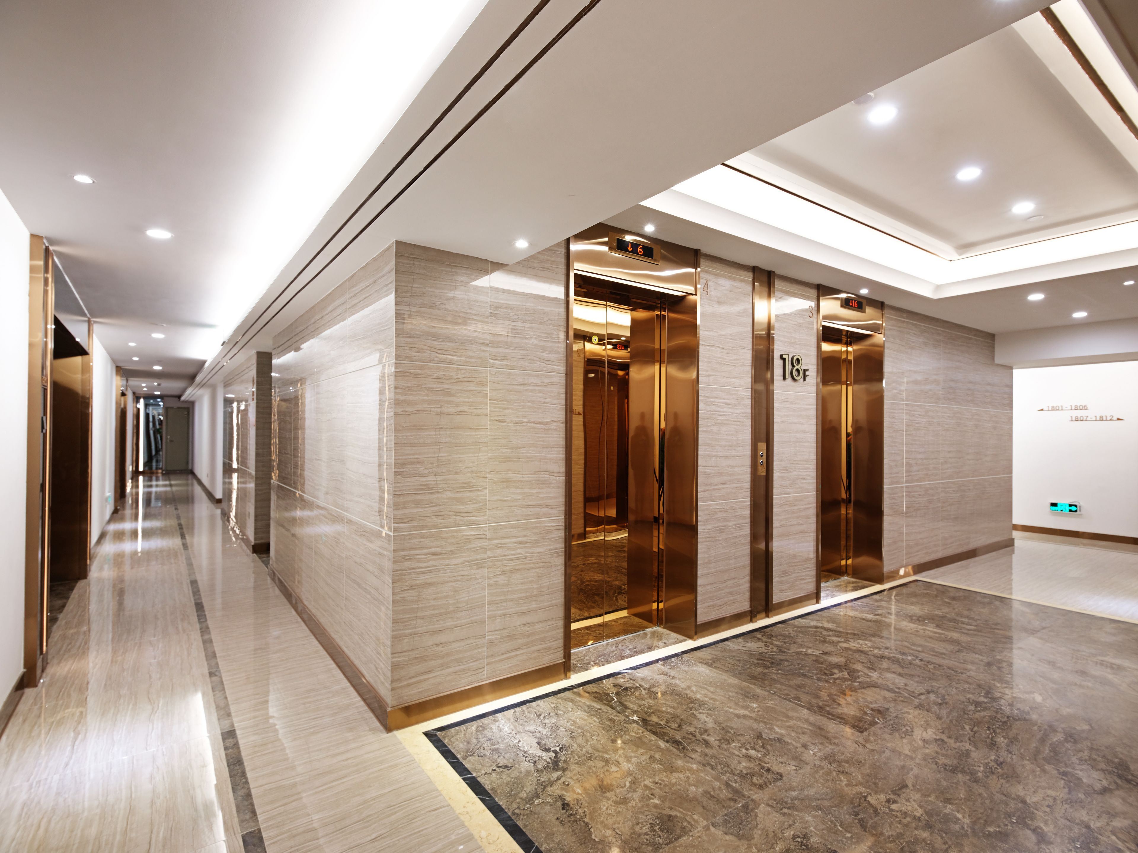 A modern hotel corridor with a marble floor, a glass elevator, and a digital display showing the floor number.