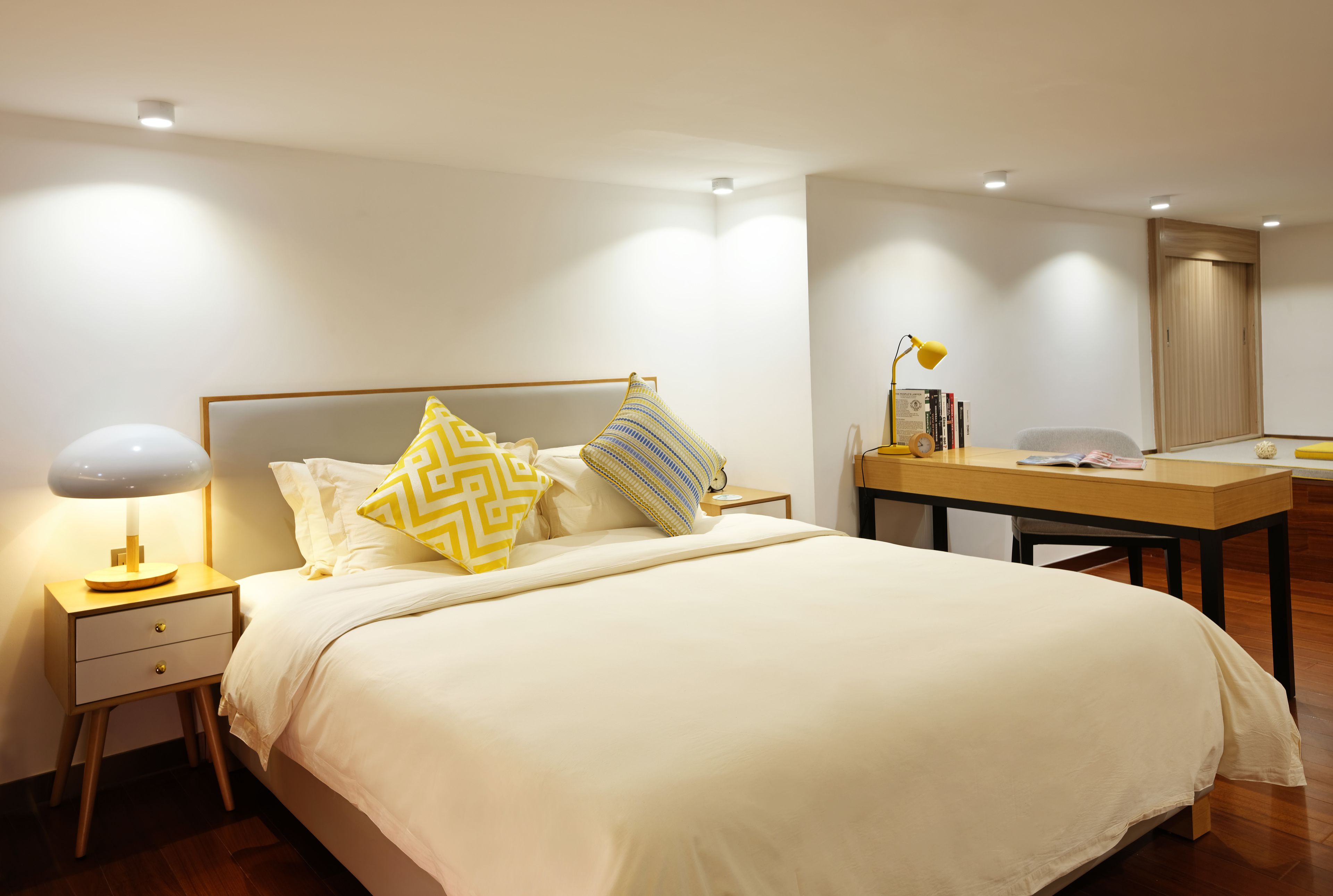 A neatly arranged bedroom with a bed, bedside table, lamp, and a desk with a chair.