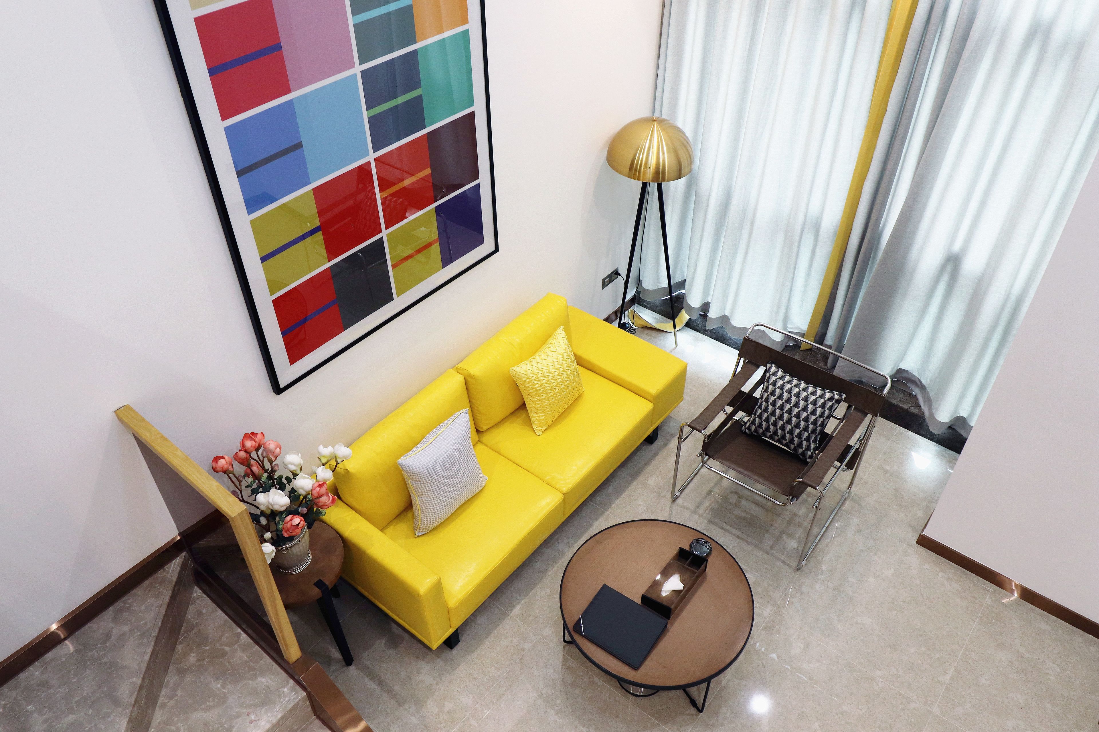 A modern living room with a yellow sofa, a round coffee table, and a floor lamp.