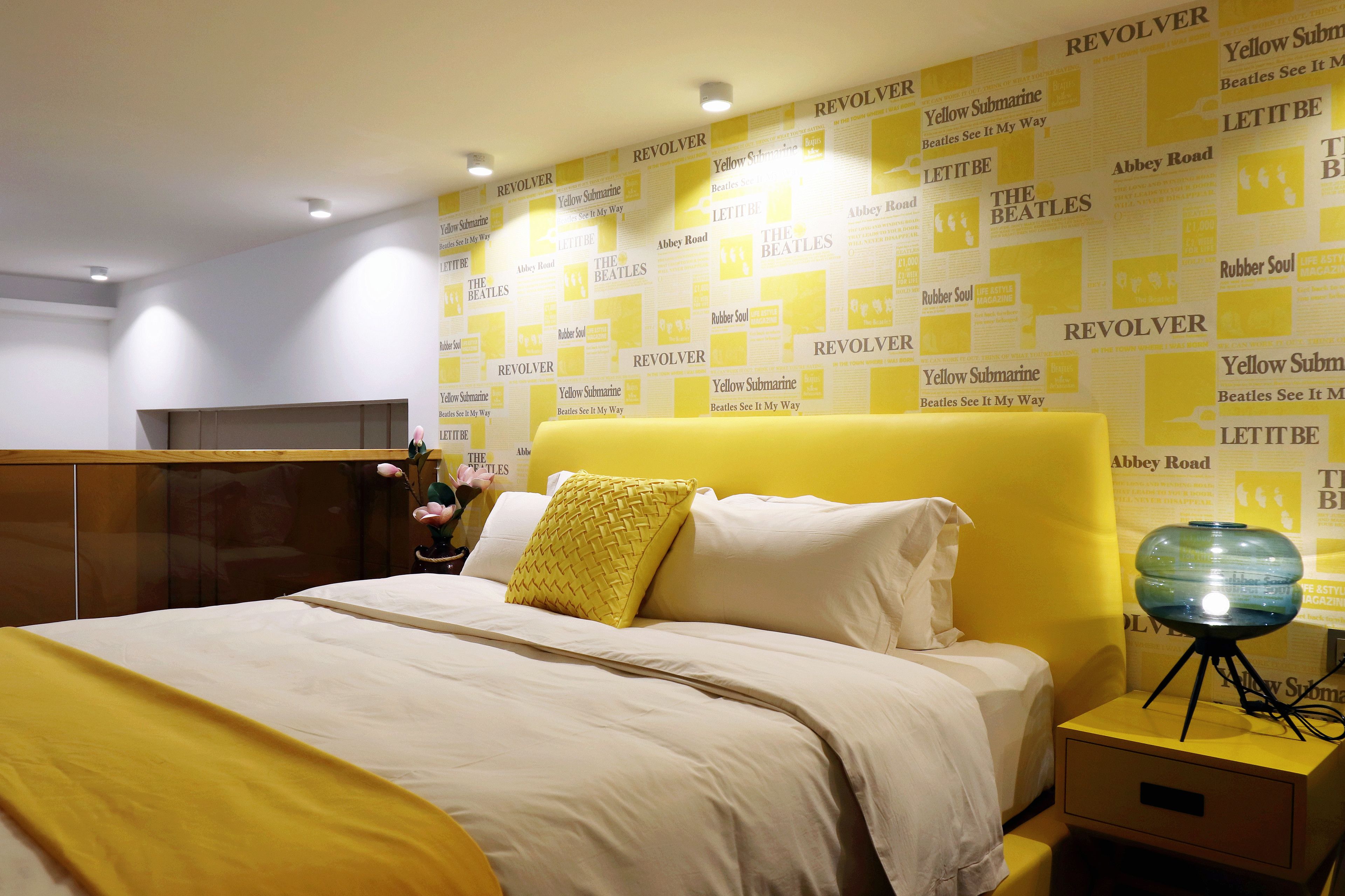 Ein Hotelzimmer mit einem Bett, einem Nachttisch und einer Wand, die mit Beatles-Postern gestaltet ist.