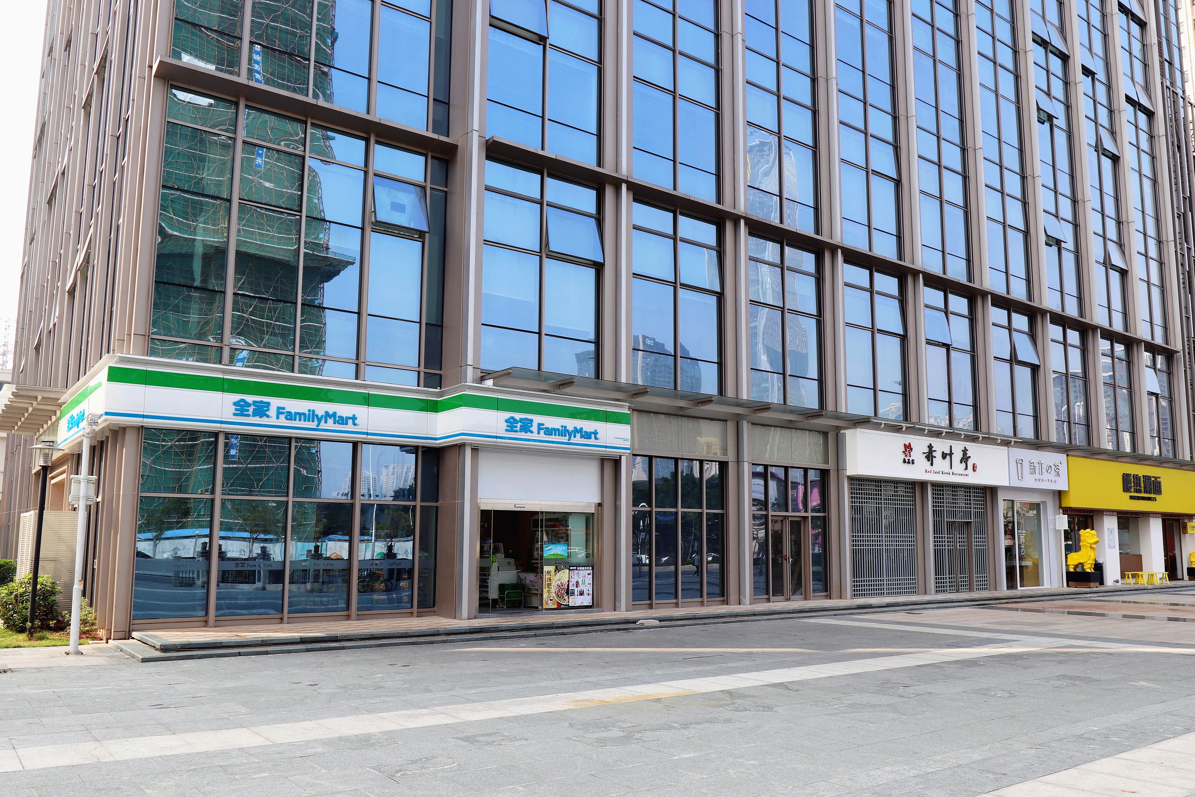 Un edificio con una tienda FamilyMart en la planta baja, ventanas grandes y un escaparate amarillo al otro lado de la calle.