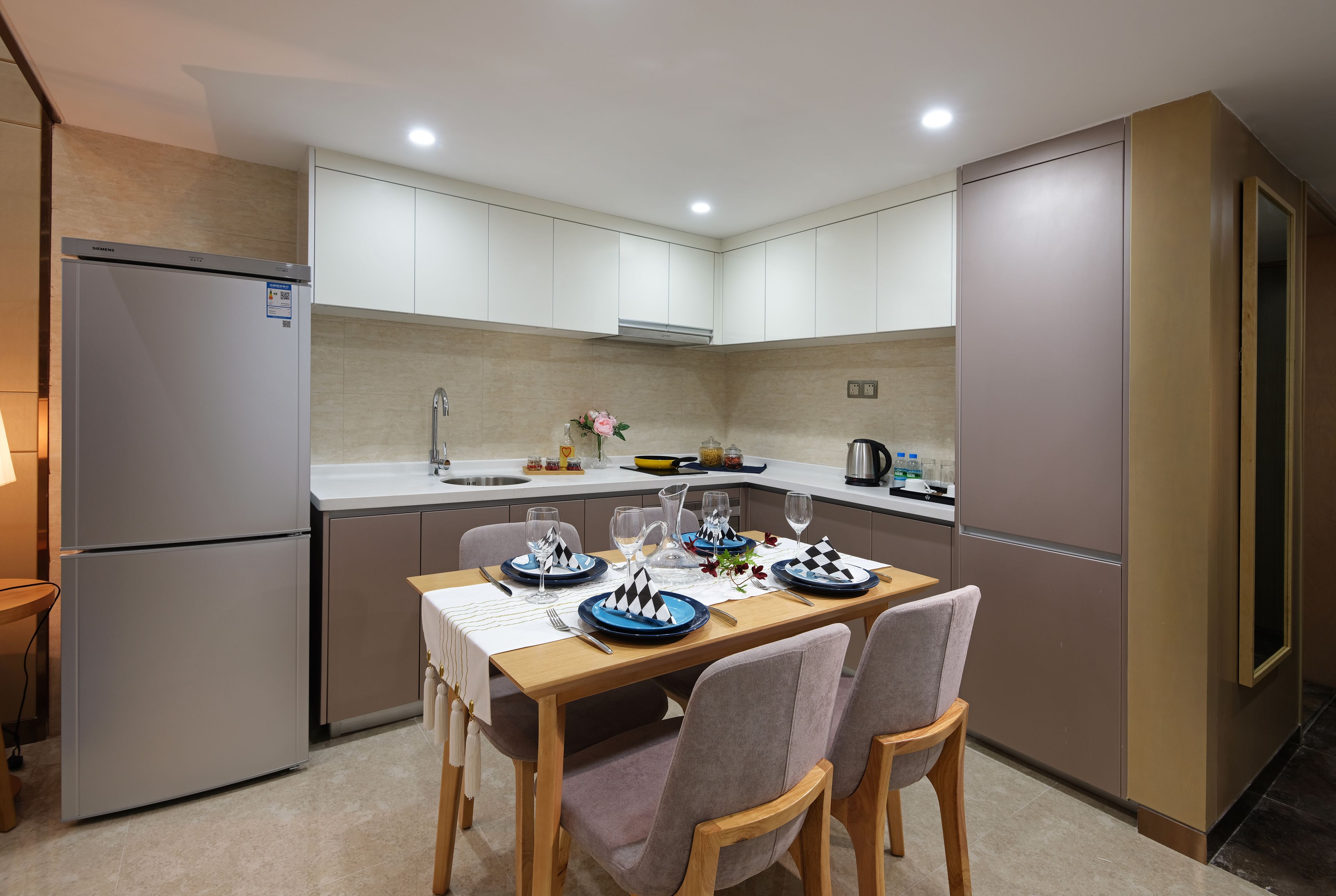 A modern kitchen with white cabinets, a built-in oven, and a dining area with a wooden table and chairs.