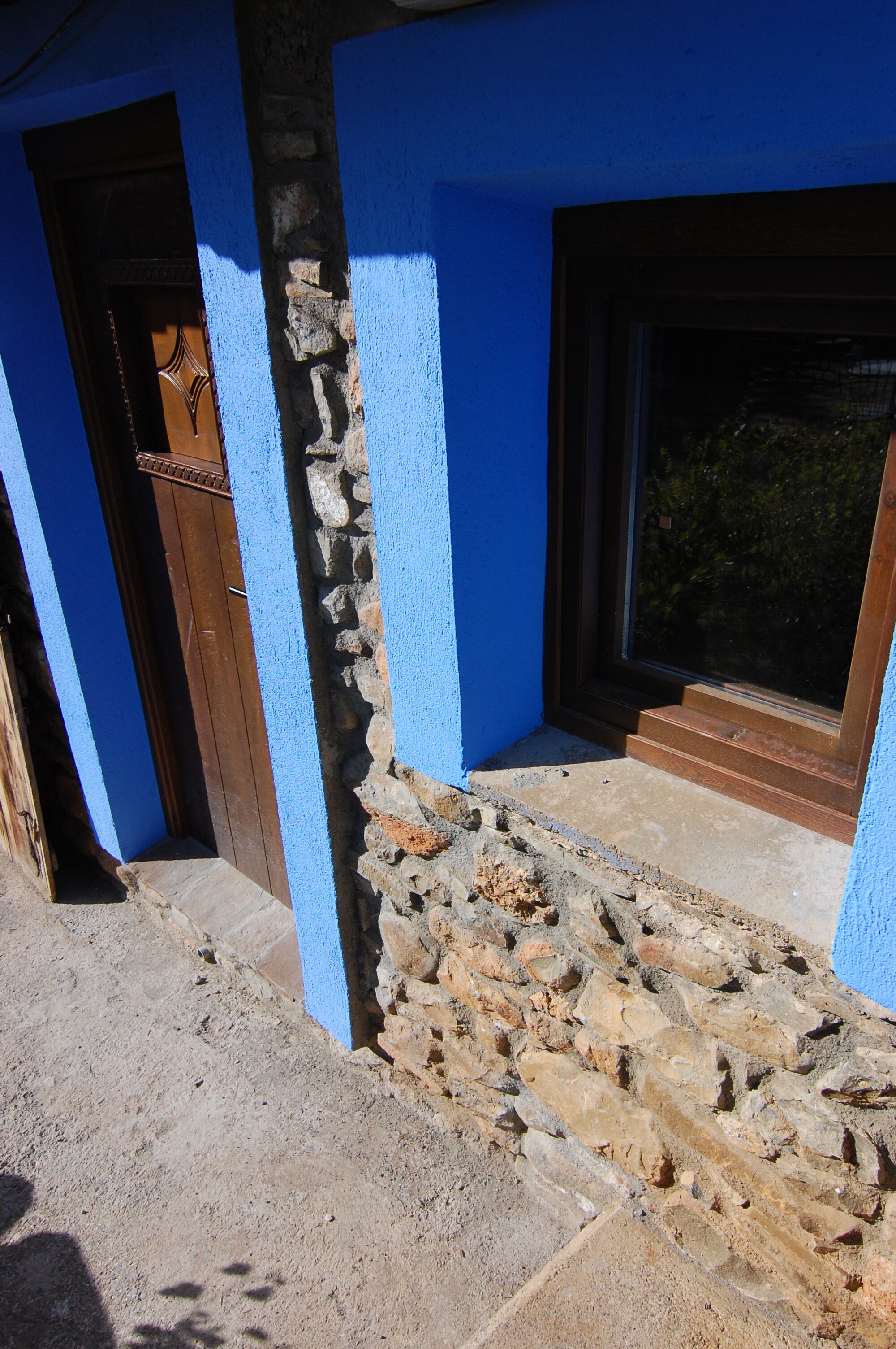 Un edificio con fachada azul, una puerta de madera y un muro de piedra.