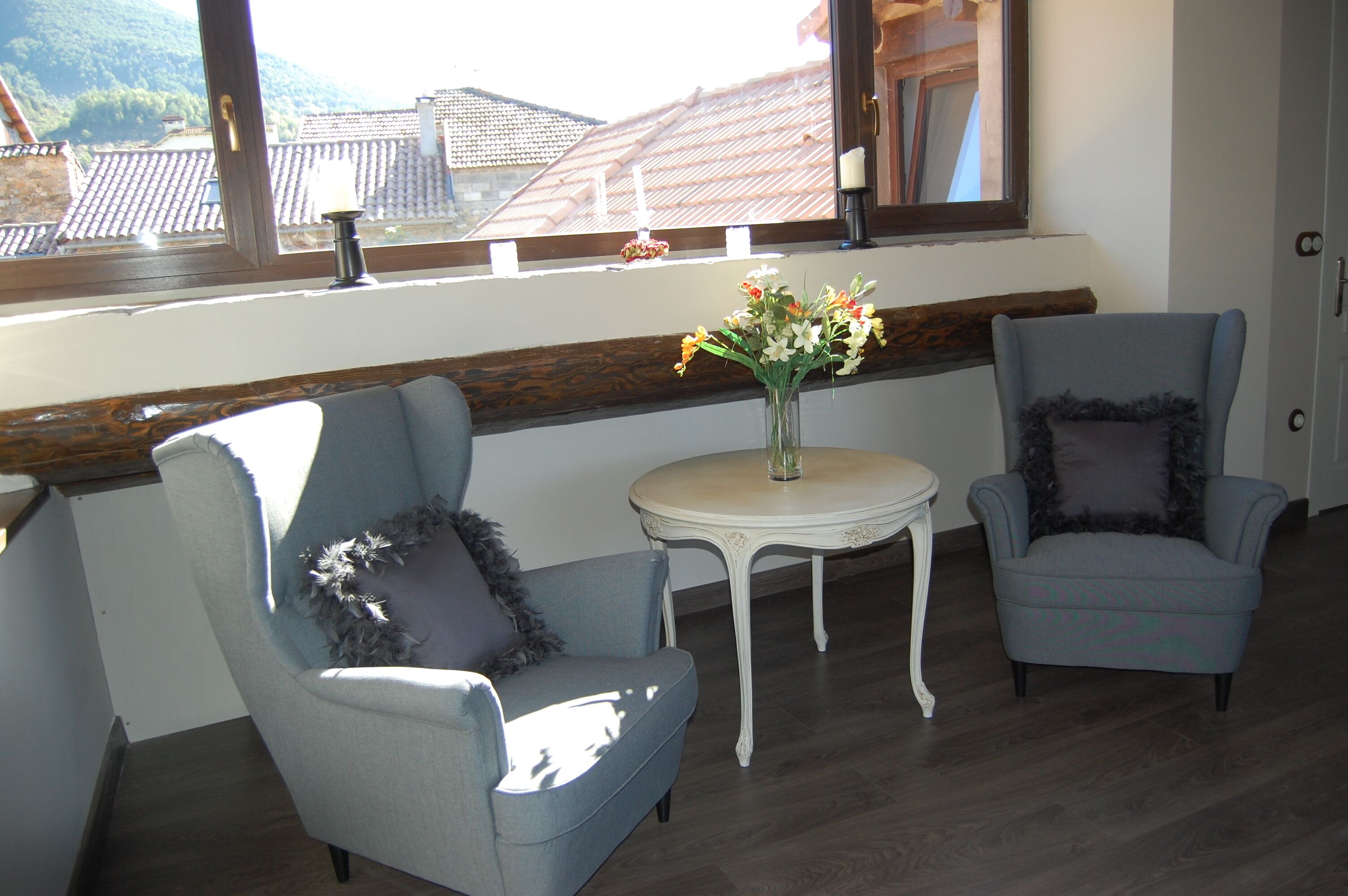 Een kamer met twee lichtblauwe fauteuils, een witte salontafel met een bloevas, en uitzicht op gebouwen door een raam met een houten vensterbank.