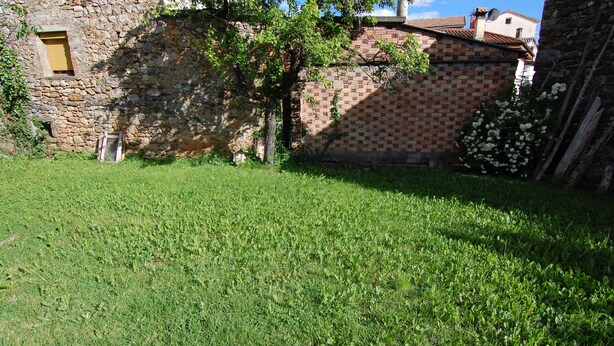 A grassy courtyard with a stone building and a brick wall. - El Capricho de Nieves (Laspuna)