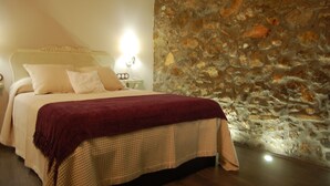 A bedroom with a stone wall, a bed with a checkered bedspread, and a red throw blanket. - El Capricho de Nieves (Laspuna)