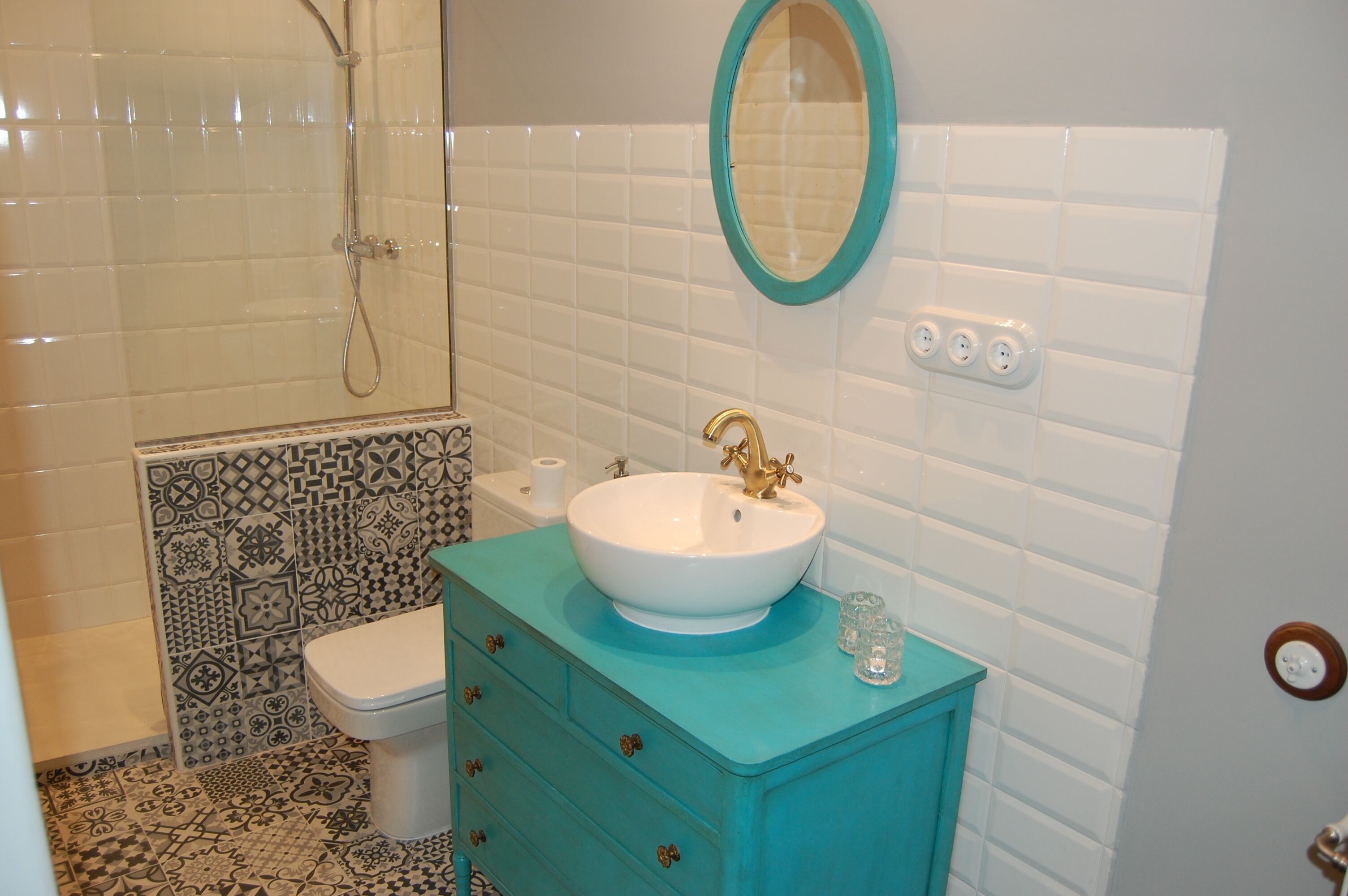 Casa de banho com lavatório branco, toucador azul-turquesa, pavimento com azulejos estampados e área de duche.