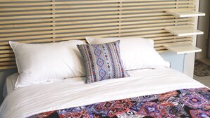 Un lit recouvert d’une couverture à motifs, un oreiller orné d’un motif géométrique et une décoration murale représentant des motifs de feuilles et le mot « FLORESCENCE ».