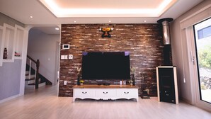 Un salon moderne doté d’un grand téléviseur à écran plat fixé à un mur en bois, d’un meuble de rangement blanc avec des tiroirs et d’une cheminée.