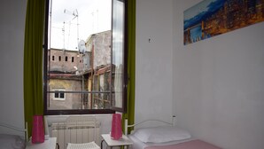 A small hotel room with a bed, a chair, a table, and a window with a view of buildings.